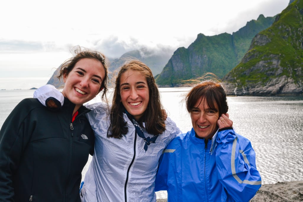 Tre ragazze sorridenti con paesaggio montuoso e acqua sullo sfondo, vacanze tra amici, Lofoten